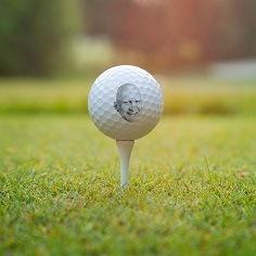 Golf ball printed with a photo of a man's face, on a tee